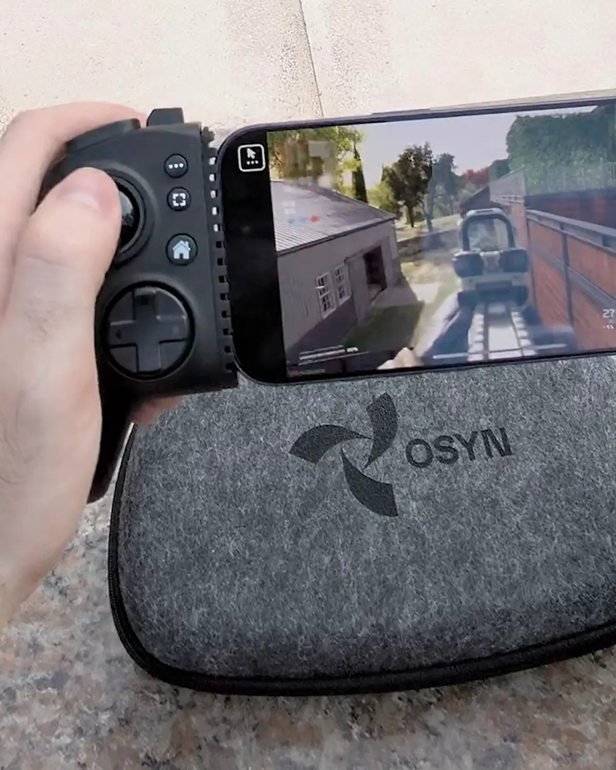 Sur une terrasse, une main tient Osyn Pro par sa poignée, téléphone en place, au-dessus de l’étui de la manette