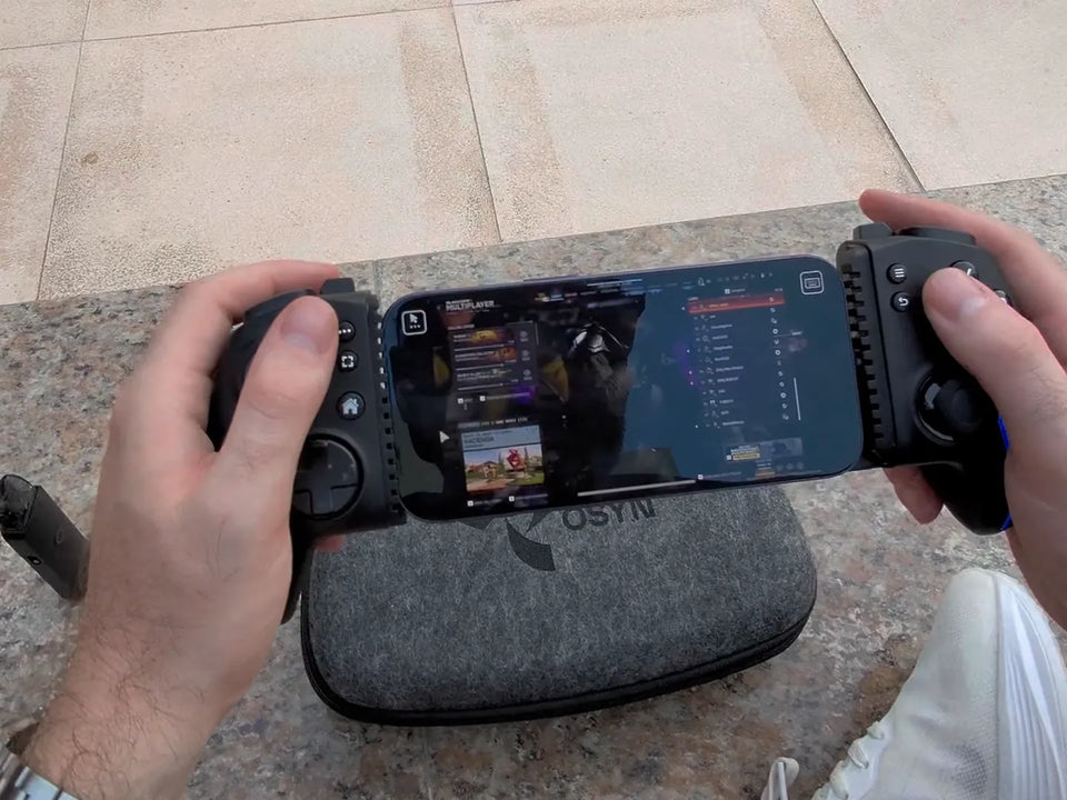 Deux mains tiennent la manette Osyn Pro pendant une partie, téléphone en place